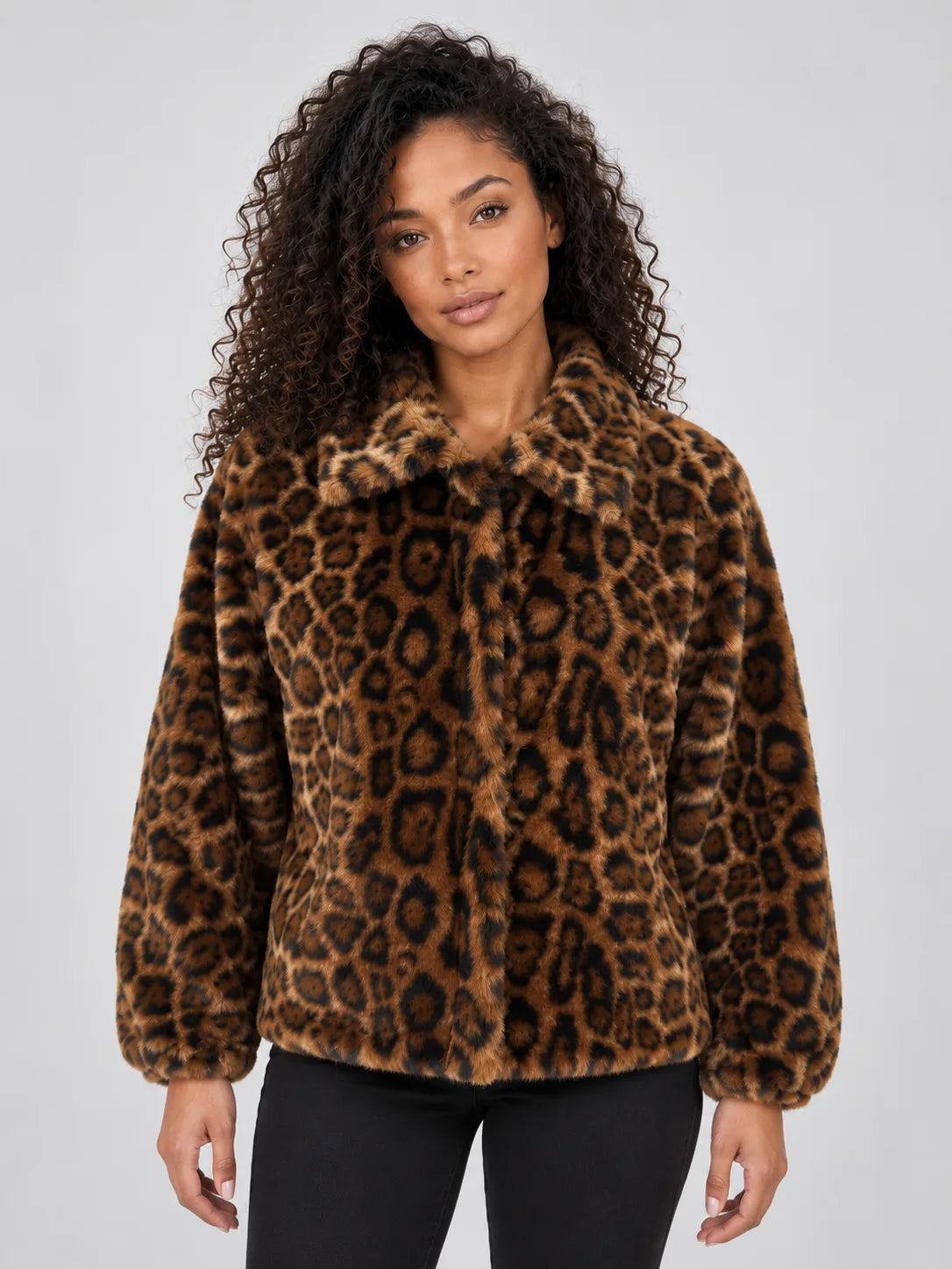 Front view of a woman wearing a plush leopard print faux fur jacket with a wide pointed collar, open over black trousers