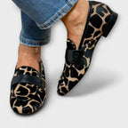 Close-up of a woman's feet wearing leopard-print pony hair loafers with a black leather saddle strap, paired with cropped jeans.