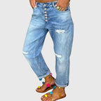 Front view of light blue distressed boyfriend jeans with exposed button fly and cuffed hems, worn with pom-pom sandals