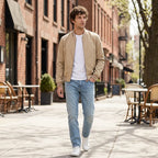 Man wearing the beige bomber jacket with jeans and white trainers, walking through a city street
