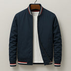 Navy bomber jacket on a hanger with red, white and navy striped ribbing at the collar and cuffs