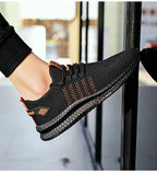 On-foot side view of black and orange knit trainer with orange striped heel tab, worn with black joggers
