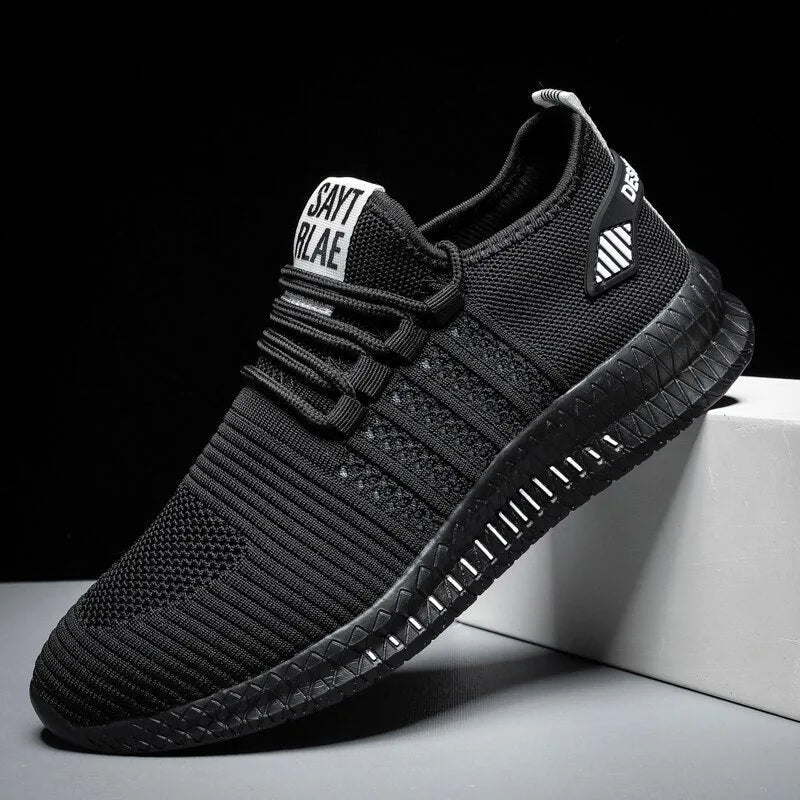 Angled side view of all-black knit trainer with white heel tab text and black ridged sole