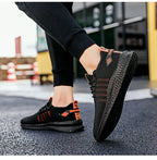 On-foot close-up of black and orange knit trainer lifted mid-step, showing textured black outsole