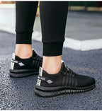 Rear view of ankles in black and white knit trainers with reflective heel tabs, walking on pavement
