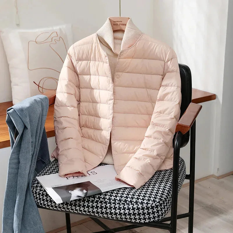 Pale pink quilted jacket with stand collar worn over a cream polo neck jumper on a chair
