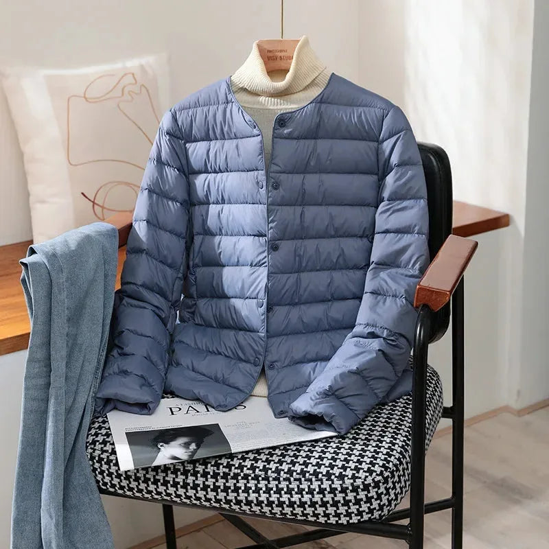 Haze blue quilted lightweight jacket with stand collar draped over a chair with denim
