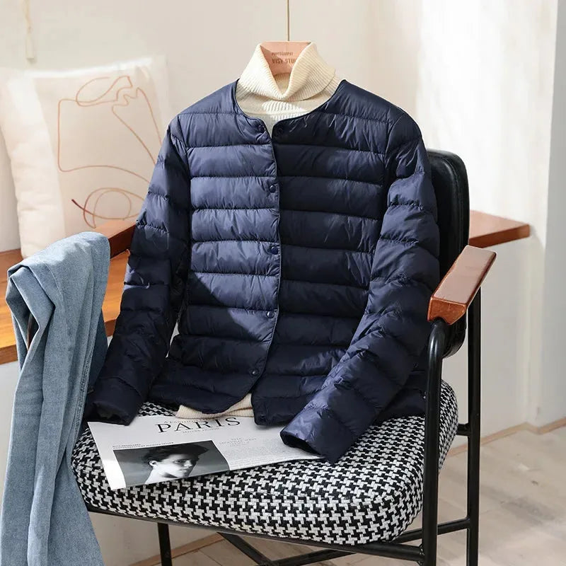 Navy blue quilted lightweight jacket with stand collar hung over a cream polo neck jumper