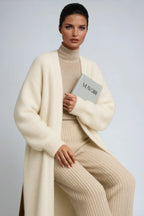 Close-up of a cream knit long cardigan worn over a matching ribbed polo neck jumper and trousers