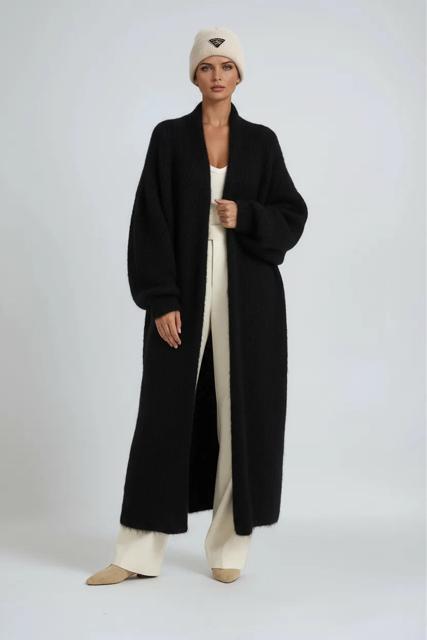 Full-length view of a woman in a black textured long cardigan layered over cream wide-leg trousers