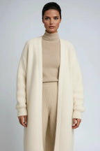 Close-up of a cream knit long cardigan with relaxed sleeves worn over a beige ribbed polo neck and trousers