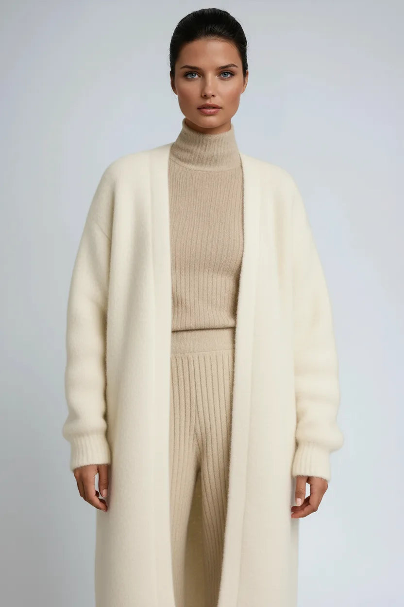 Close-up of a cream knit long cardigan with relaxed sleeves worn over a beige ribbed polo neck and trousers