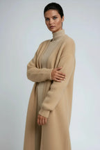 Side profile of a woman in a camel long cardigan with arms crossed, showing the relaxed oversized sleeve