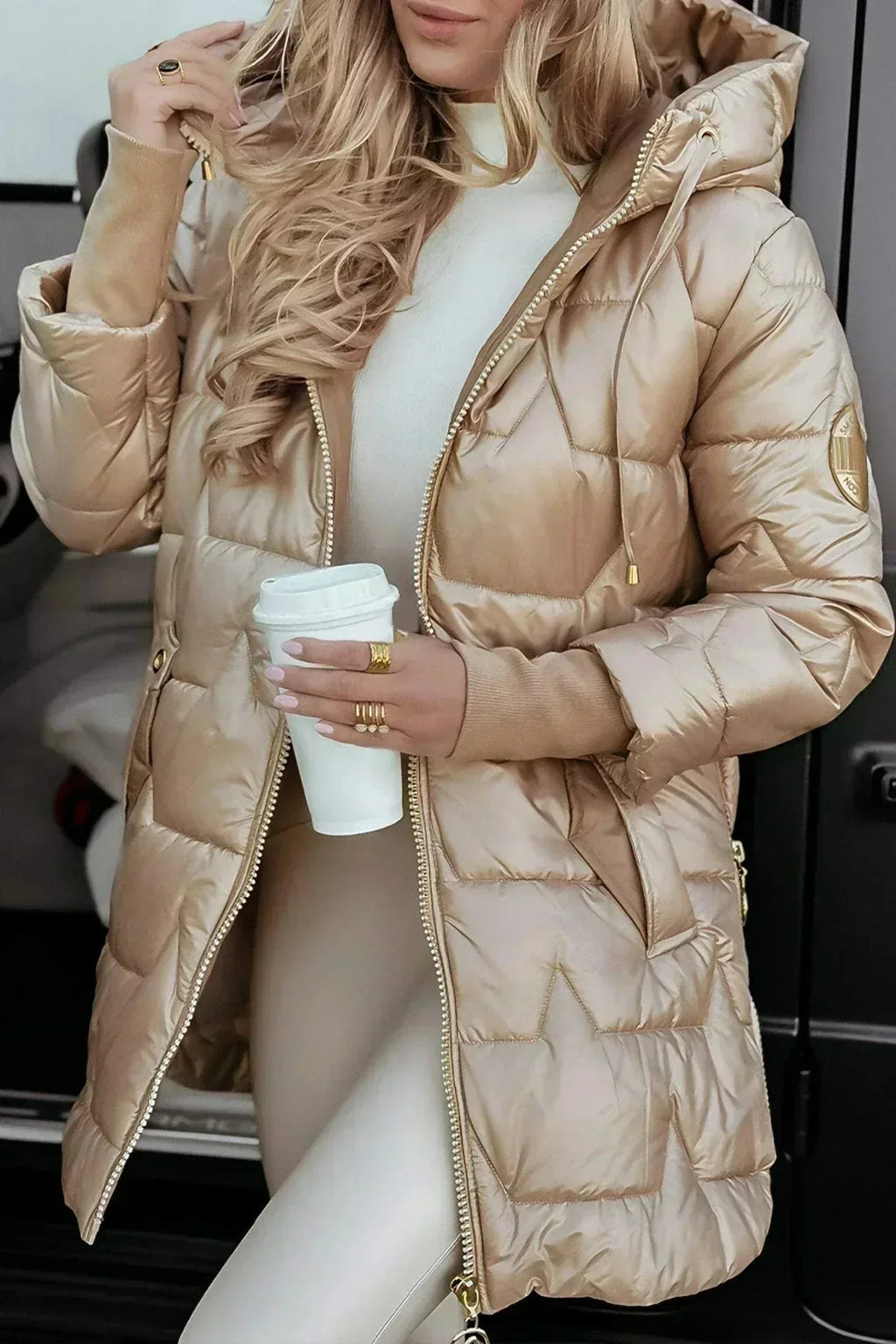 Close-up of a grey metallic puffer coat with hood and drawstring detail, worn open over a white jumper