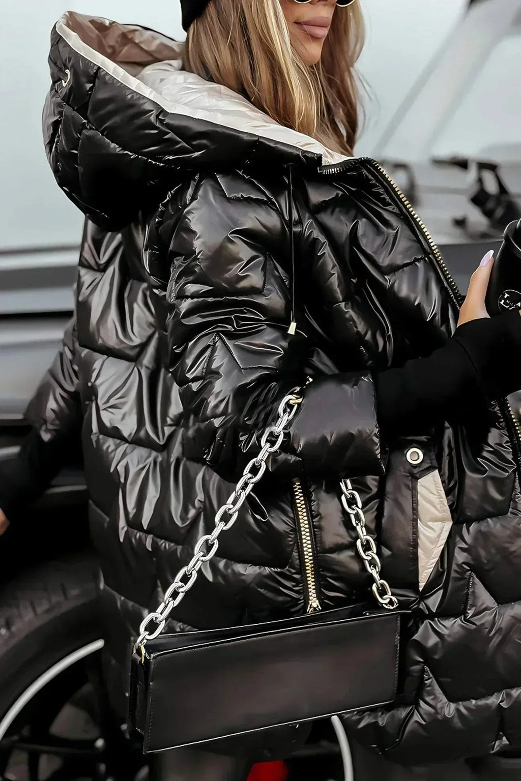 Woman in a glossy black puffer coat with contrast beige lining, holding a drink and a black handbag