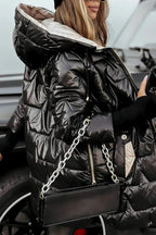 Woman in a glossy black puffer coat with contrast beige lining, holding a drink and a black handbag