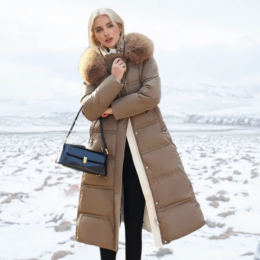 Woman in long brown puffer coat with oversized fur hood holding a black handbag on a snowy landscape
