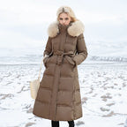 Front view of brown longline puffer coat with fur-trimmed hood and matching tie belt over black trousers
