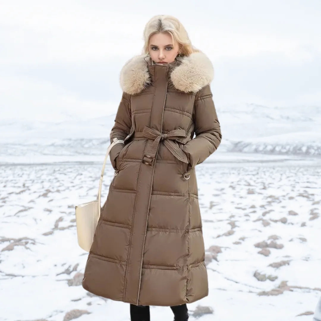 Front view of brown longline puffer coat with fur-trimmed hood and matching tie belt over black trousers