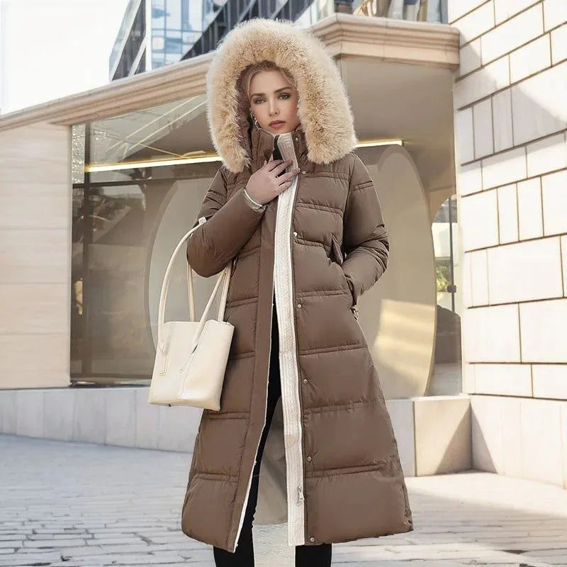 Model in brown quilted maxi coat with fur hood standing on a sunlit city street holding a cream tote bag