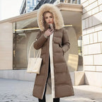 Model in brown quilted maxi coat with fur hood standing on a sunlit city street holding a cream tote bag