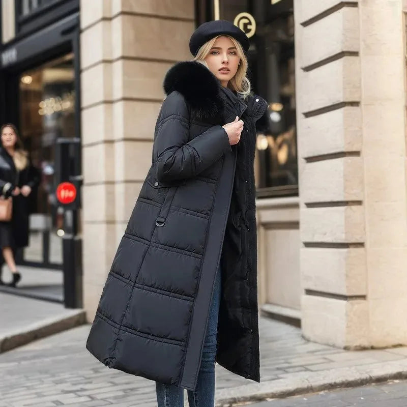 Side angle of black quilted maxi coat with black fur hood worn on a stone-paved city street