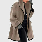 Beige longline coat with black contrast trim, relaxed silhouette layered over dark trousers
