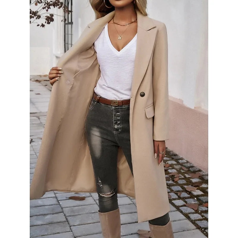 Beige longline tailored coat worn open with a leather belt visible at the waist over dark jeans