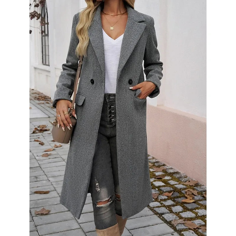 Woman in a dark grey longline coat carrying a small crossbody bag while walking outdoors