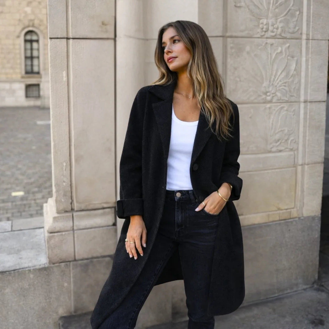 Woman in a black longline wool coat buttoned at the front, paired with a white top and jeans