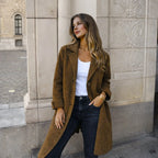 Woman standing against a stone wall wearing a longline wool coat with classic lapels and button fastening