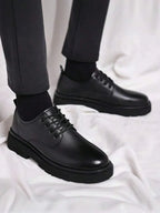 Side view of men's black leather derby shoes worn with dark grey tailored trousers and black socks.