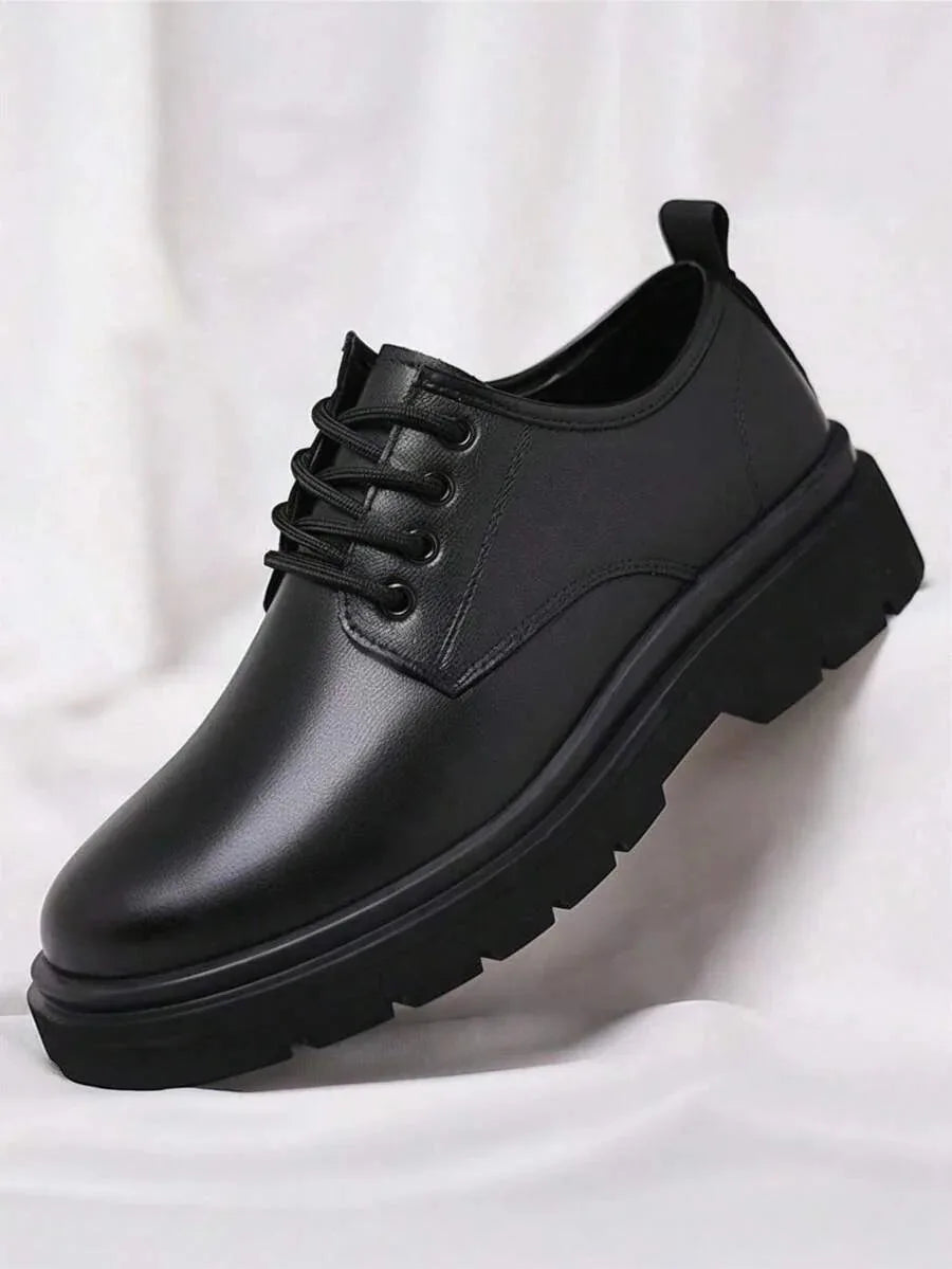 Angled close-up of a single black leather derby shoe showing lace-up front, round toe and chunky ridged sole.