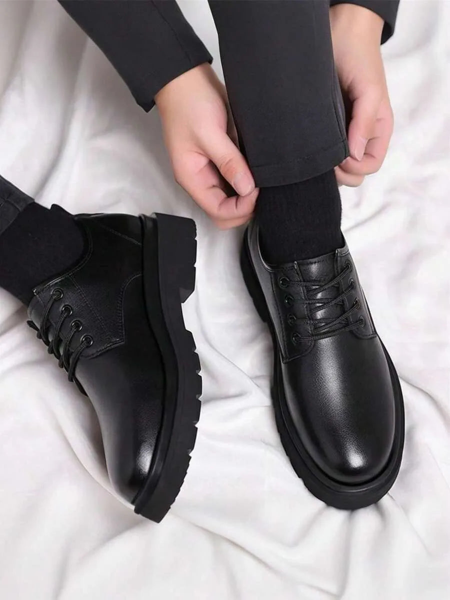 Overhead view of a hand adjusting a sock above a pair of black leather lace-up derby shoes on a white backdrop.