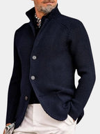 Man wearing a navy ribbed knit cardigan with stand collar, button front and hand in trouser pocket