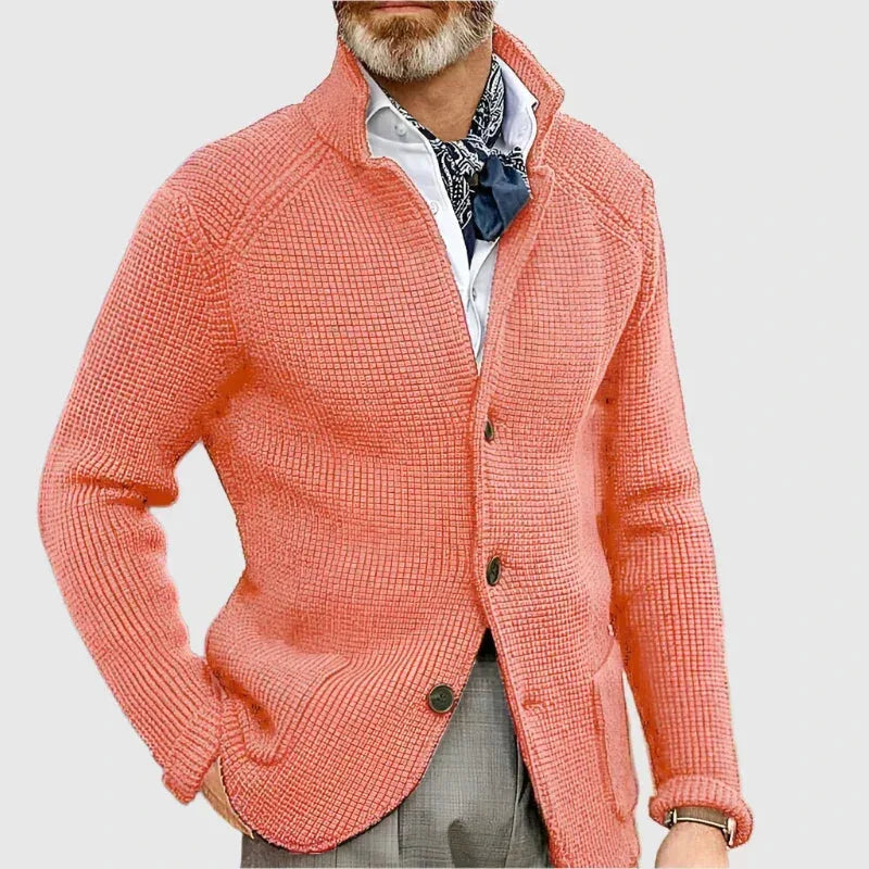 Man with hands in pockets wearing the navy knit cardigan with white trousers, three-quarter view