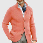 Man with hands in pockets wearing the navy knit cardigan with white trousers, three-quarter view