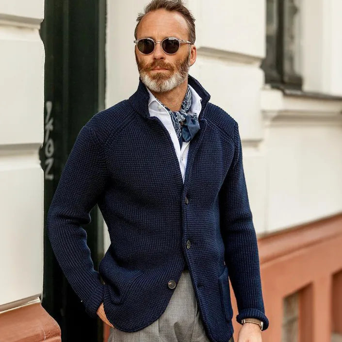 Man styling the navy knit cardigan open over a shirt and neckerchief with grey tailored trousers