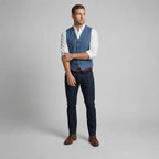 Full-length front view of a man in a blue waistcoat with crossed arms, paired with dark denim and brown boots