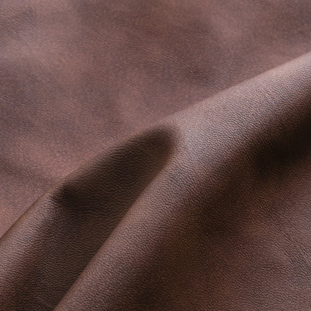 Macro shot of brown leather surface showing natural grain and soft folded texture