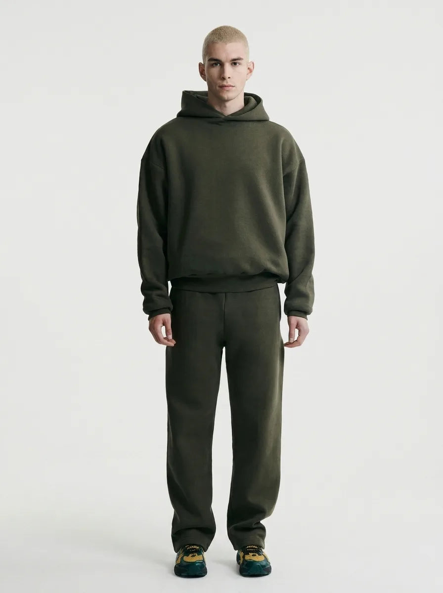 Front view of a man wearing an oversized olive green hoodie and matching jogger set with multicoloured trainers
