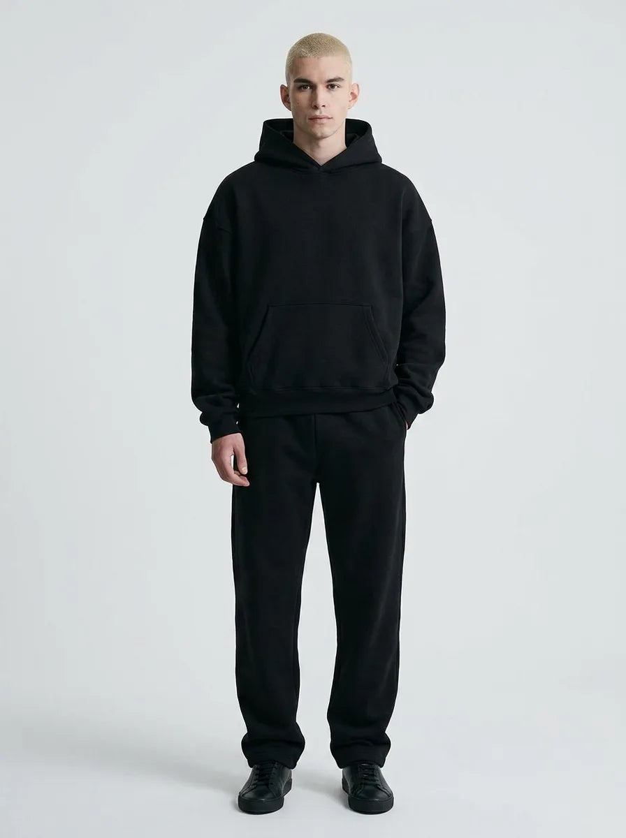 Front view of a man in a plain black oversized hoodie and jogger tracksuit paired with black trainers