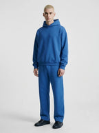 Man wearing a cobalt blue hooded sweatshirt and matching relaxed-fit joggers with black trainers