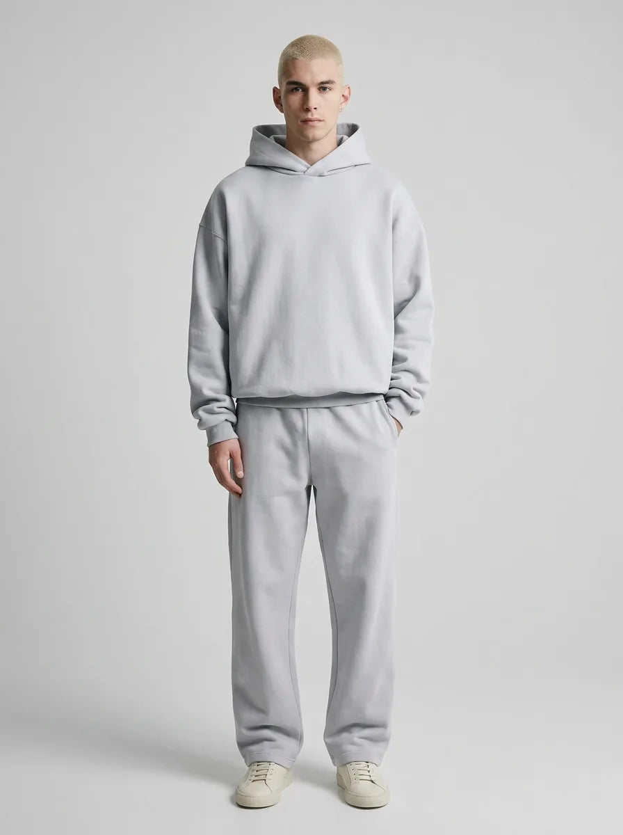 Man wearing a light grey hooded sweatshirt and joggers set styled with white trainers