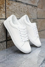 Side profile of white trainers with lace-up front, leaning against a stone tiled wall