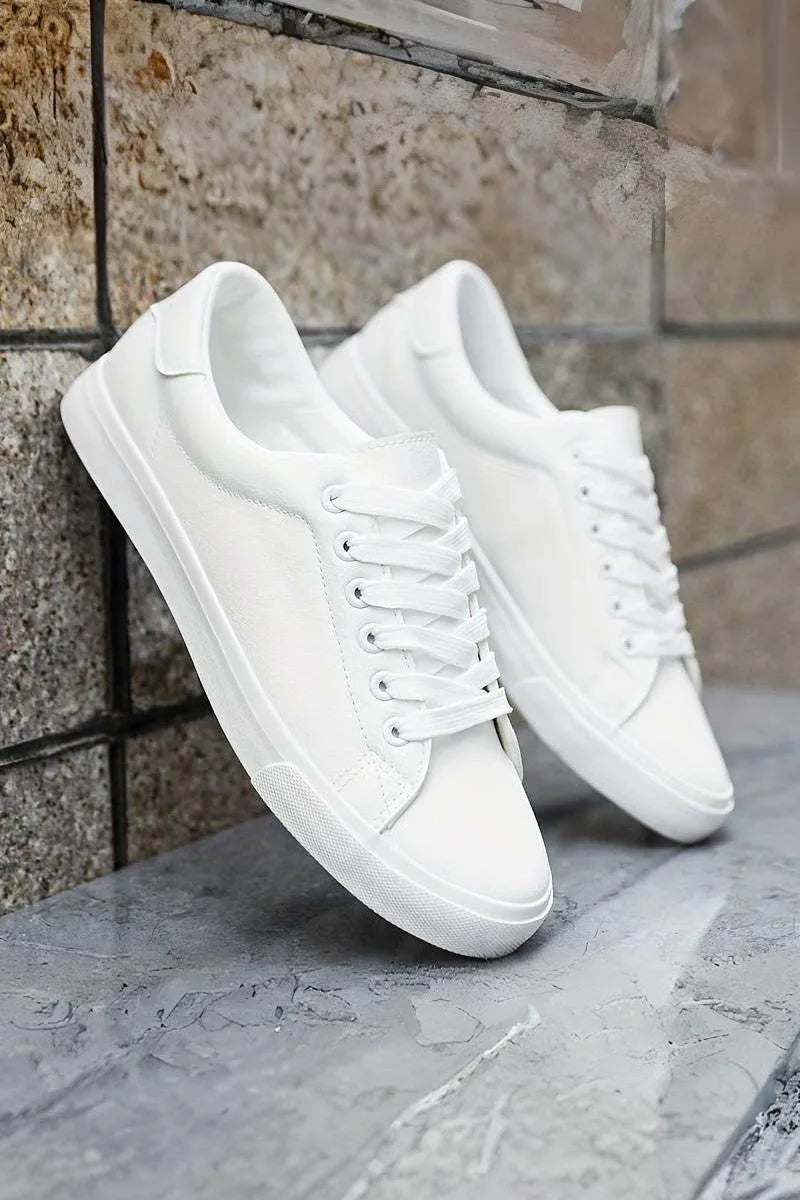 Side profile of white trainers with lace-up front, leaning against a stone tiled wall