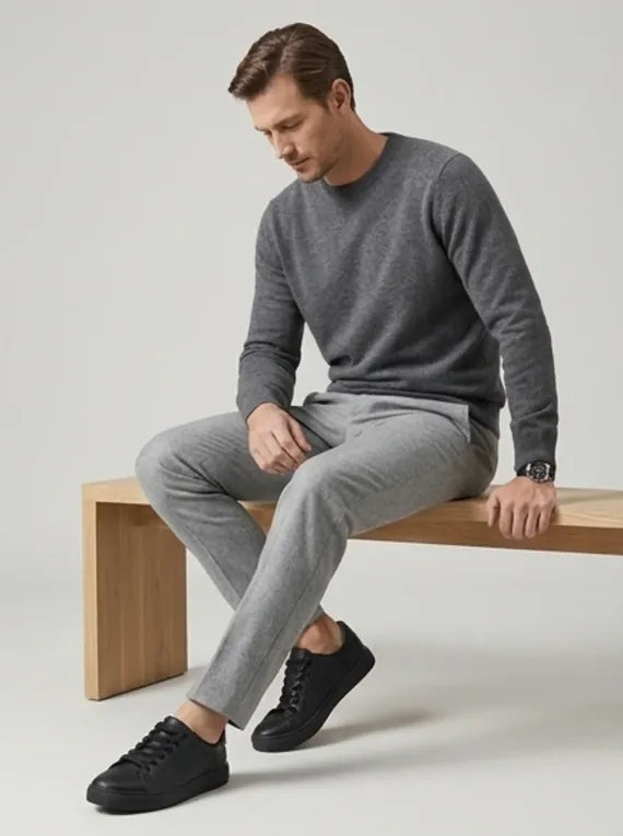 Man seated on a wooden bench wearing grey jumper, trousers and black trainers