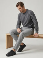 Man seated on a wooden bench wearing grey jumper, trousers and black trainers
