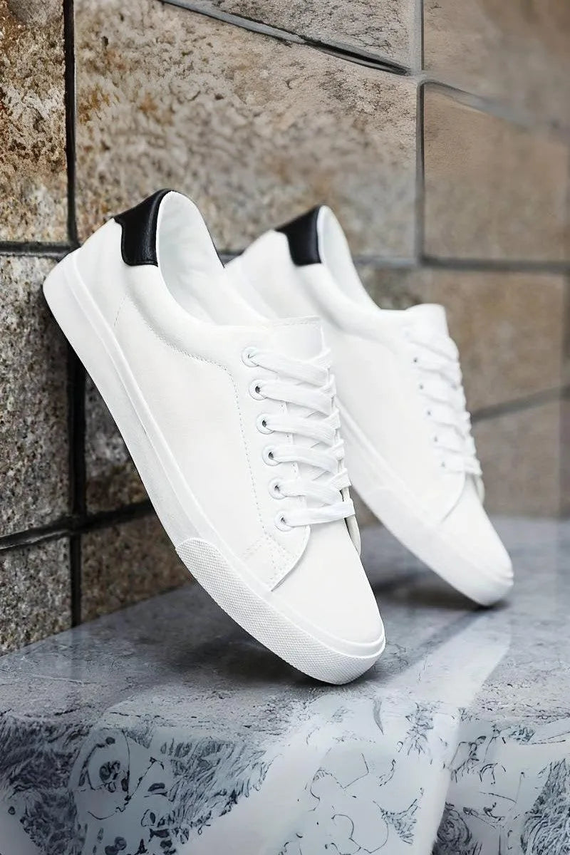Pair of white trainers with contrasting black heel tab resting on a marble surface