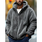 Man wearing a grey fluffy fleece zip-up hoodie with hands in the pockets, paired with jeans for a casual look